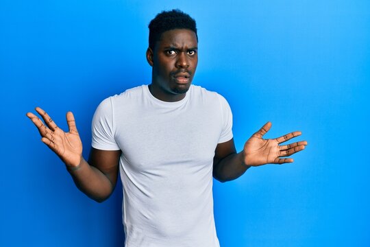 Handsome black man wearing casual white t shirt clueless and confused with open arms, no idea and doubtful face.