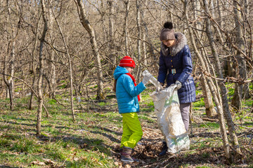 Naklejka na ściany i meble A girl throws a plastic bottle into a trash bag that the girl holds, together they collect garbage in the forest