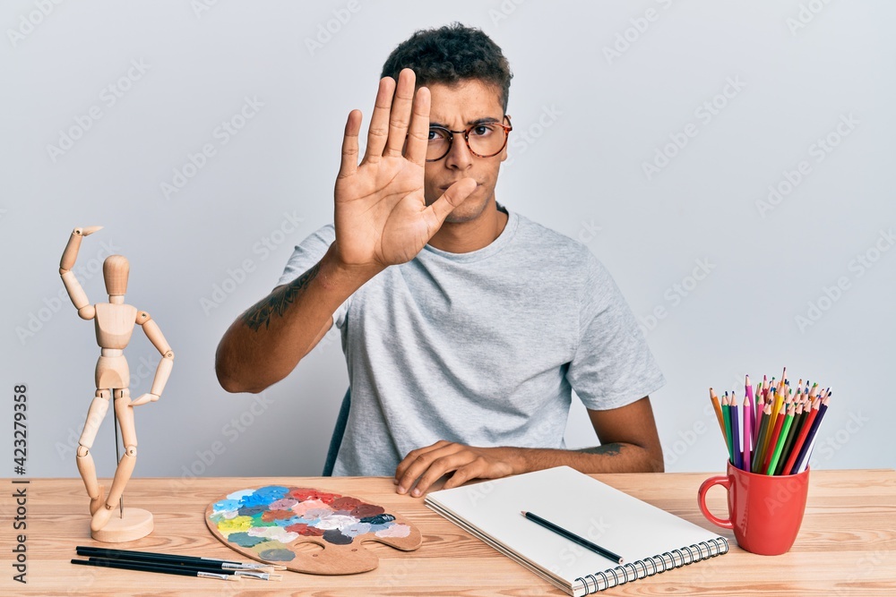 Poster young handsome african american man painter sitting palette and art manikin doing stop sing with pal