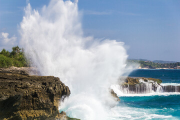 Big powerful waves hitting rocks throwing water in the air spraying black rocky coastline, Indonesia, Nusa Lembongan