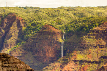 Waterfall and Waimea canyon, with red soil and green trees, Kauai, Hawaii