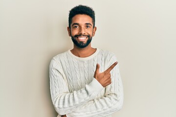Handsome hispanic man with beard wearing casual winter sweater smiling cheerful pointing with hand and finger up to the side