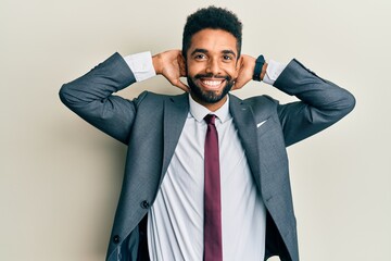 Handsome hispanic man with beard wearing business suit and tie relaxing and stretching, arms and hands behind head and neck smiling happy