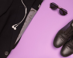 Flat set of womens clothing such as black suit, black shoes, glasses on pink background. View from above.