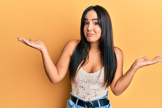 Young beautiful hispanic girl wearing casual clothes clueless and confused with open arms, no idea and doubtful face.