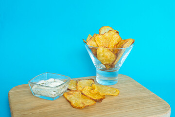 Fresh baked homemade potato chips in a glass bowl on a board with dipping source. Crispy potato...