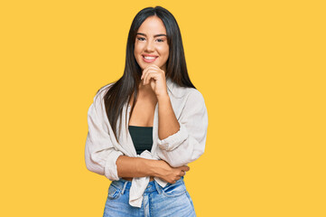 Young beautiful hispanic girl wearing casual clothes looking confident at the camera smiling with crossed arms and hand raised on chin. thinking positive.