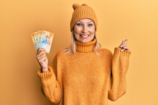 Middle age caucasian woman holding swiss franc banknotes smiling happy pointing with hand and finger to the side