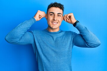 Hispanic young man wearing casual winter sweater smiling pulling ears with fingers, funny gesture....