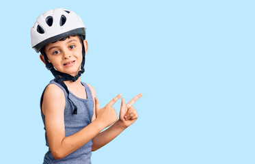 Little cute boy kid wearing bike helmet smiling and looking at the camera pointing with two hands and fingers to the side.