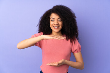 Young african american woman isolated on purple background holding copyspace imaginary on the palm...