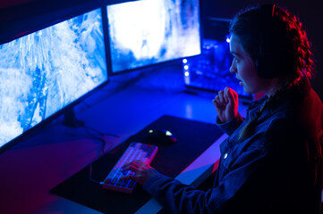 Girl gamer playing at the computer in shooters, steam. Neon light, e-sports and computer games industry