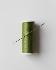 The spool of green thread and needle on the white background.