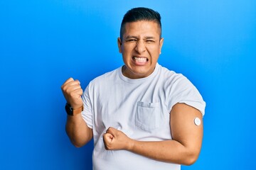 Young latin man using glucose meter button screaming proud, celebrating victory and success very...