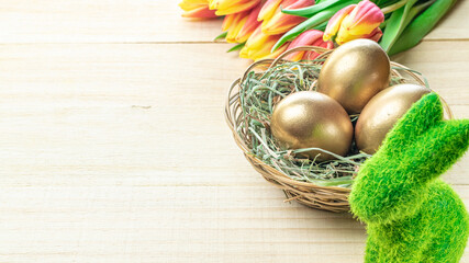 Easter egg. Happy Easter decoration: Golden eggs in basket with spring tulips, white feathers on wooden background. Traditional decoration in sun light.