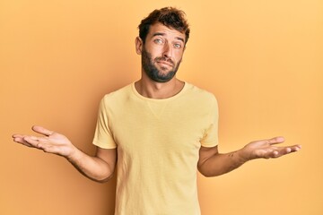 Handsome man with beard wearing casual yellow tshirt over yellow background clueless and confused...