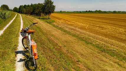 Summer landscape of the Venetian plain. Orange bicycle on the dirt road near a wheat field after harvest. Warm sunny day.