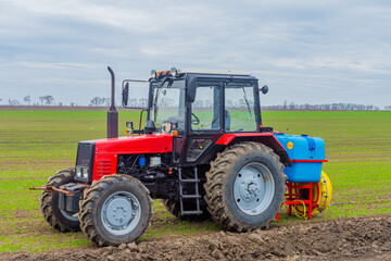 Agricultural tractor in the field with sown winter wheat. The tractor is designed to spray pesticides on crops.