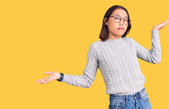 Young beautiful chinese girl wearing casual clothes clueless and confused expression with arms and hands raised. doubt concept.