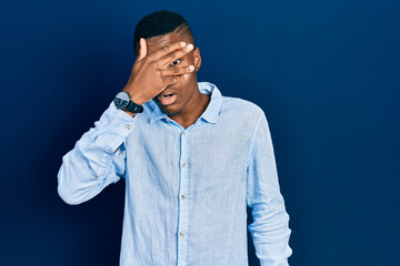 Young african american man wearing casual clothes peeking in shock covering face and eyes with hand, looking through fingers with embarrassed expression.