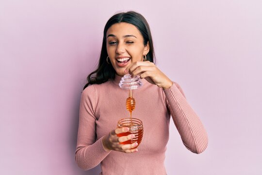 Young hispanic woman holding honey winking looking at the camera with sexy expression, cheerful and happy face.