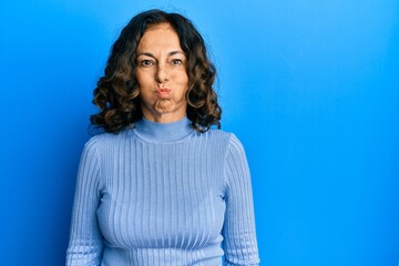 Middle age hispanic woman wearing casual clothes puffing cheeks with funny face. mouth inflated with air, crazy expression.