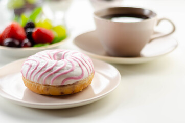 Delicious doughnut topped with white and pink icing served with coffee and fresh fruits