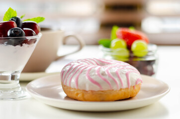 Delicious doughnut topped with white and pink icing served with coffee and fresh fruits