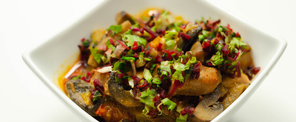 A thick stew of meat, potatoes, mushrooms, and mix of peppers served in a white bowl
