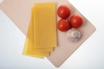 Foto op Plexiglas Uncooked lasagna sheets and tomatoes on wooden cutting board © RaymondZ