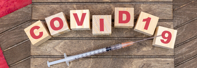 covid 19 word with letters on wooden cubes and wood background and inject for Covid-19 vaccination in the vaccination centre
