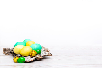 Easter colorful painted organic eggs on tree bark, spring, food, easter concept on wooden white background with copy space