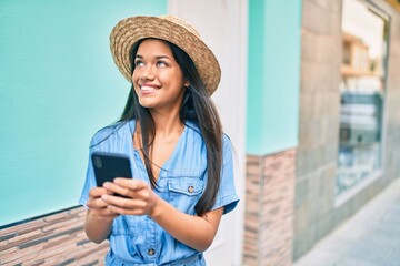 Young latin tourist girl on vacation smiling happy using smartphone at the city.