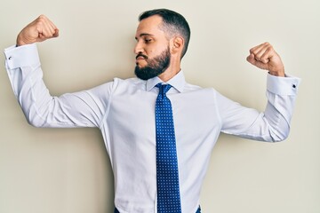 Young man with beard wearing business tie showing arms muscles smiling proud. fitness concept.