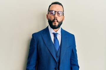 Young man with beard wearing business suit and tie making fish face with lips, crazy and comical...