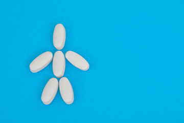 Small human figure laid out from white oblong pills on blue background. Human skeleton.