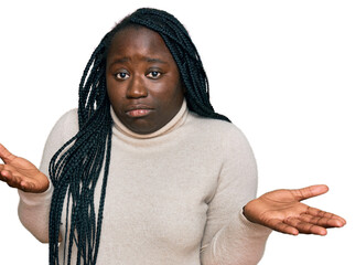 Young black woman with braids wearing casual winter sweater clueless and confused expression with arms and hands raised. doubt concept.