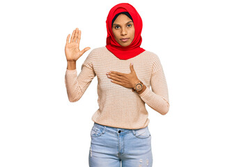 Young african american woman wearing traditional islamic hijab scarf swearing with hand on chest and open palm, making a loyalty promise oath