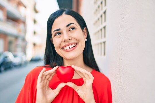 Young latin girl smiling happy holding heart at the city.
