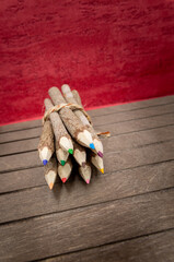 Naklejka premium bound crayons made of untreated, real wood, unique and with real tree bark on a wooden board and red background for nature topics, students and artists