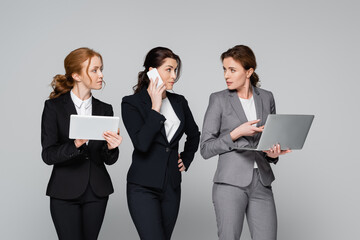 Businesswomen in formal wear using gadgets isolated on grey