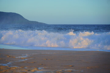 Ondas quebrando no mar na Praia de Piratininga, Niterói no Rio de Janeiro. Morro ao fundo. Fim de tarde de verão.