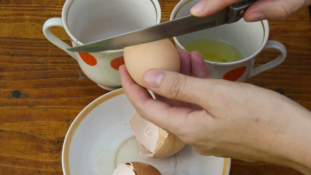 Raw Organic Egg With Brown Eggshell Holding In Fingers Before Breaking With Kitchen Knife. POV Preparation Of Food Ingredient For Cooking Ang Baking. Retro Crockery Plate On Background