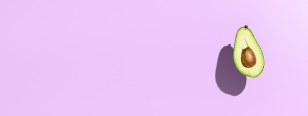 Half avocado, hovering over pastel purple color background. Minimal banner with copy space, top view