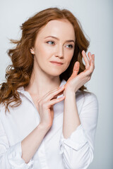 Red haired woman touching hand isolated on grey