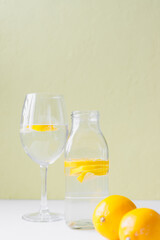 glass bottle and glass goblet with water and lemon on a light background. Lemonade, lemon juice, citrus, orange, vitamins, diet, detox, cleansing, smoothie, fresh morning, water