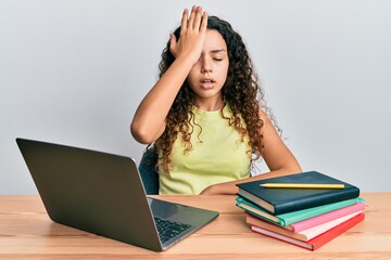 Teenager hispanic girl sitting on the table studying for school surprised with hand on head for mistake, remember error. forgot, bad memory concept.