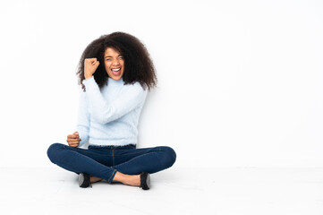 Young african american woman sitting on the floor doing strong gesture