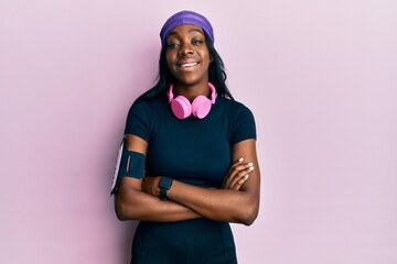 Young african american woman wearing gym clothes and using headphones happy face smiling with crossed arms looking at the camera. positive person.