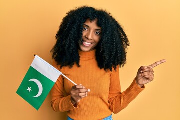 African american woman with afro hair holding pakistan flag smiling happy pointing with hand and finger to the side